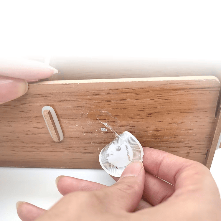 توضح الصورة تمزق ملصق RFID هش دائري وتركه بقايا عند نزعه عن سطح صندوق خشبي.