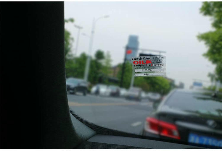 منظر من داخل سيارة يوضح ملصق RFID استاتيكي لتذكير تغيير الزيت مثبتاً على الزجاج الأمامي أمام السائق.