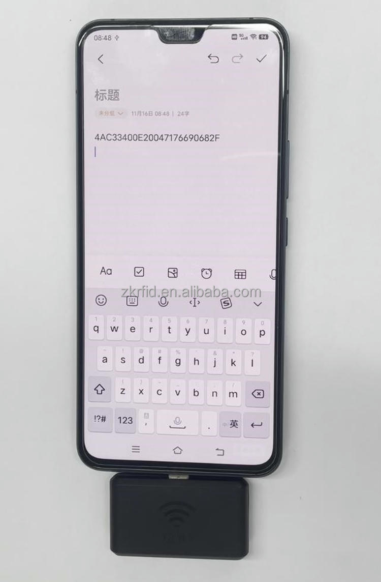 يُثبت قارئ RFID المحمول ZK-RFID-9KC بهاتف بينما يظهر نص الرمز الممسوح على الشاشة خلال عرض مباشر للإدخال.